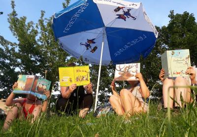 Eine Gruppe Personen liest Bücher unter einem Sonnenschirm